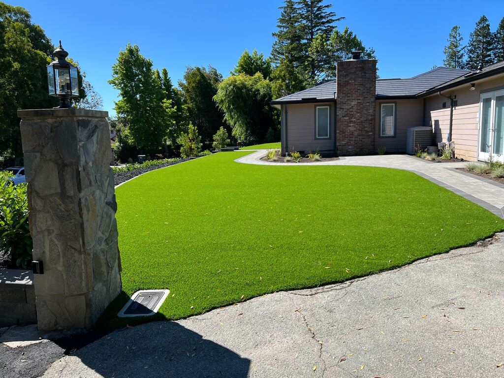 Artificial-turf lawn beside the stone entry pillar and lantern, edged by a curved paver walkway.
