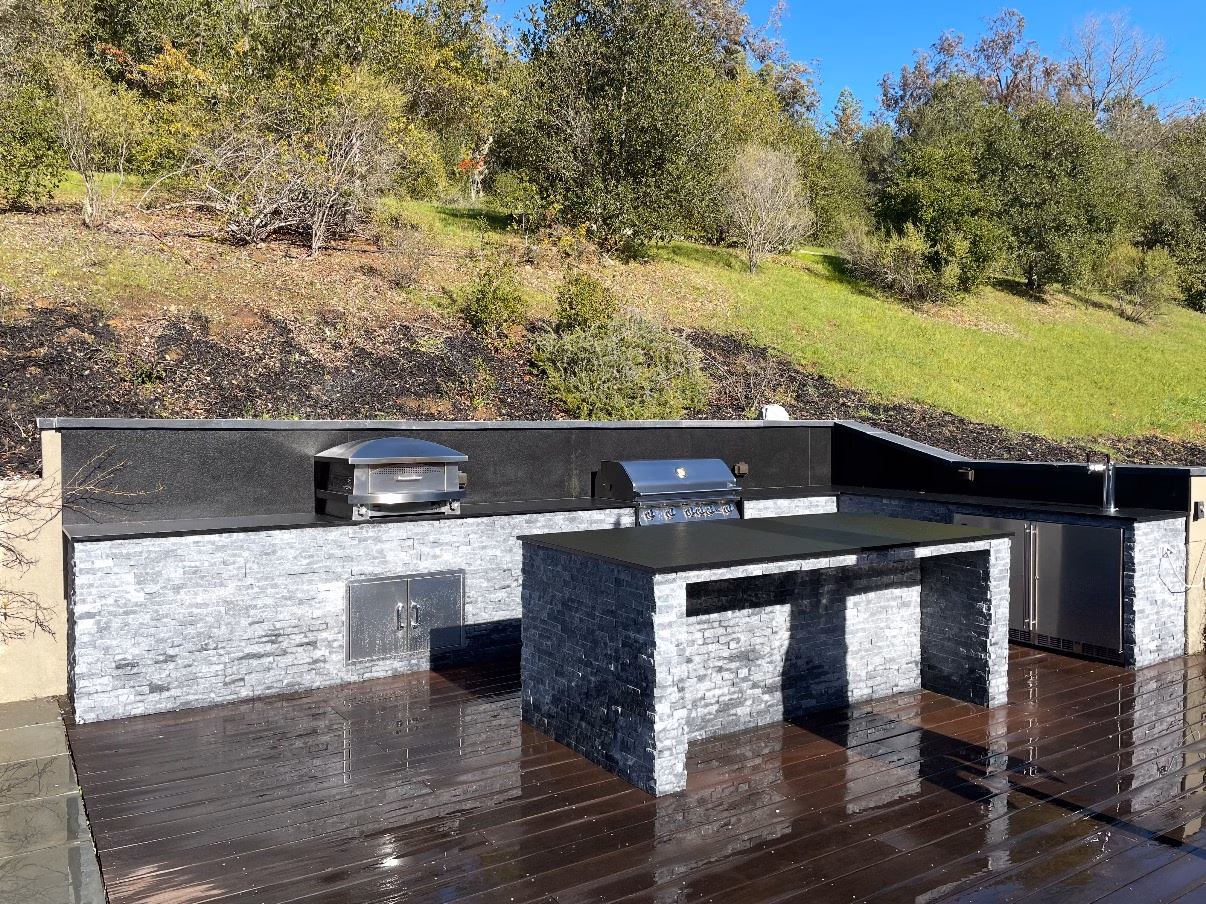 Stacked-stone outdoor kitchen and island with grills on a composite deck beside a pool, in Woodside, CA
