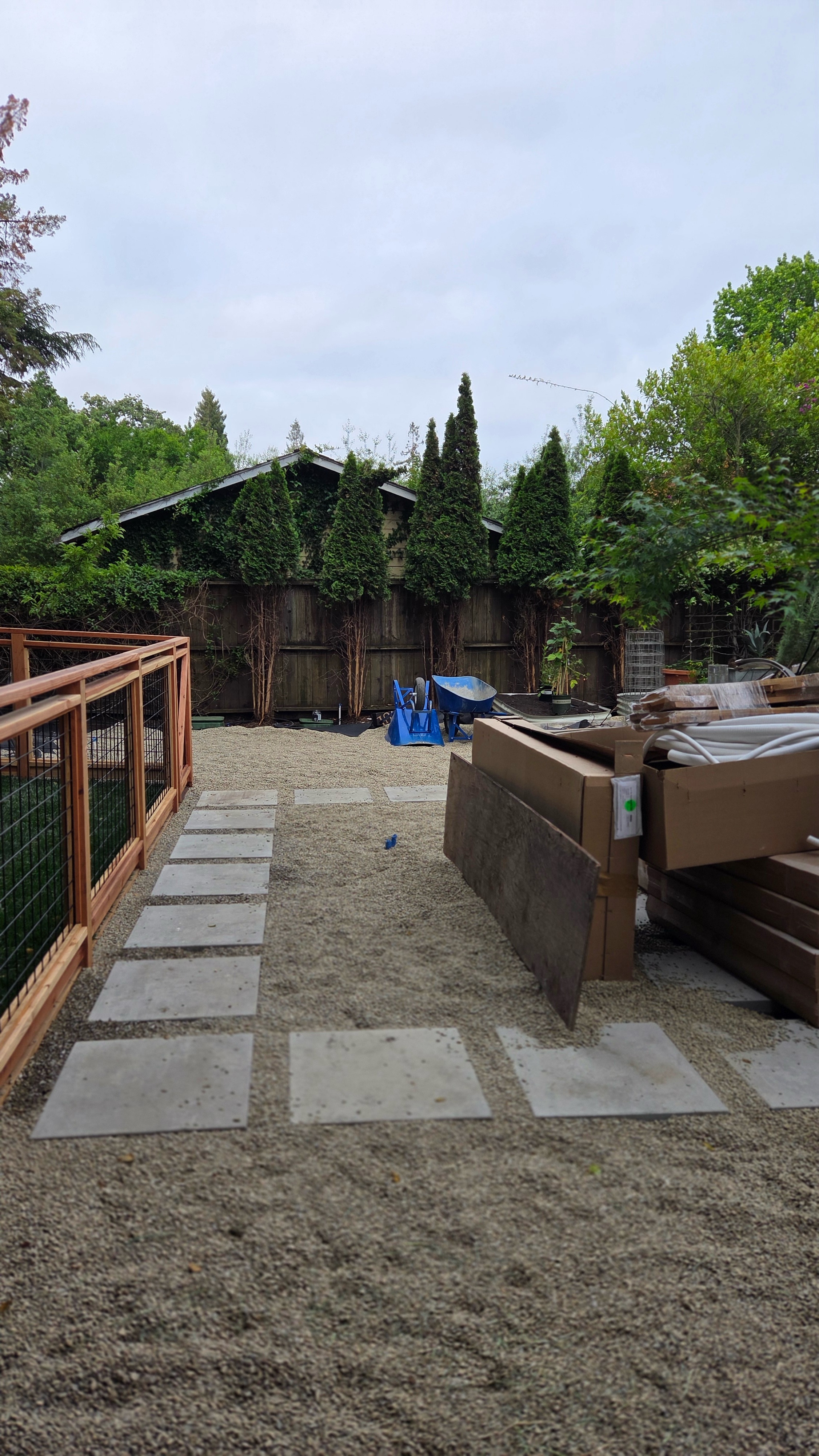 Setting concrete steppingstones over the gravel base with fencing materials staged nearby.