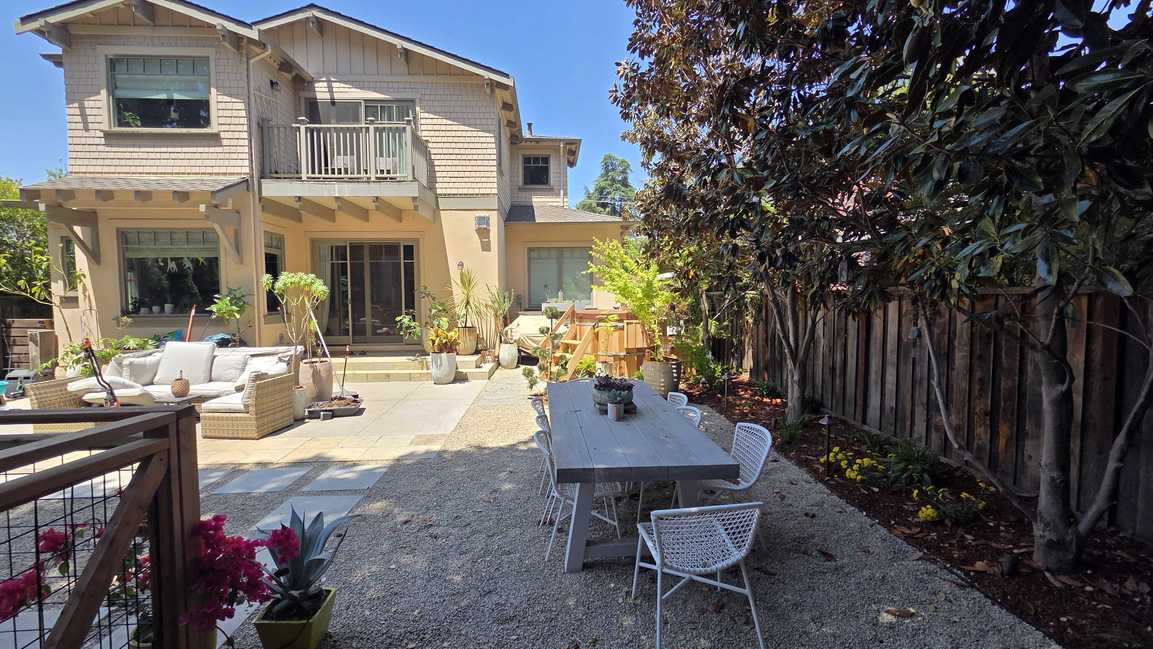 Gravel courtyard with a paver patio, a dining set, and potted plantings behind the house.