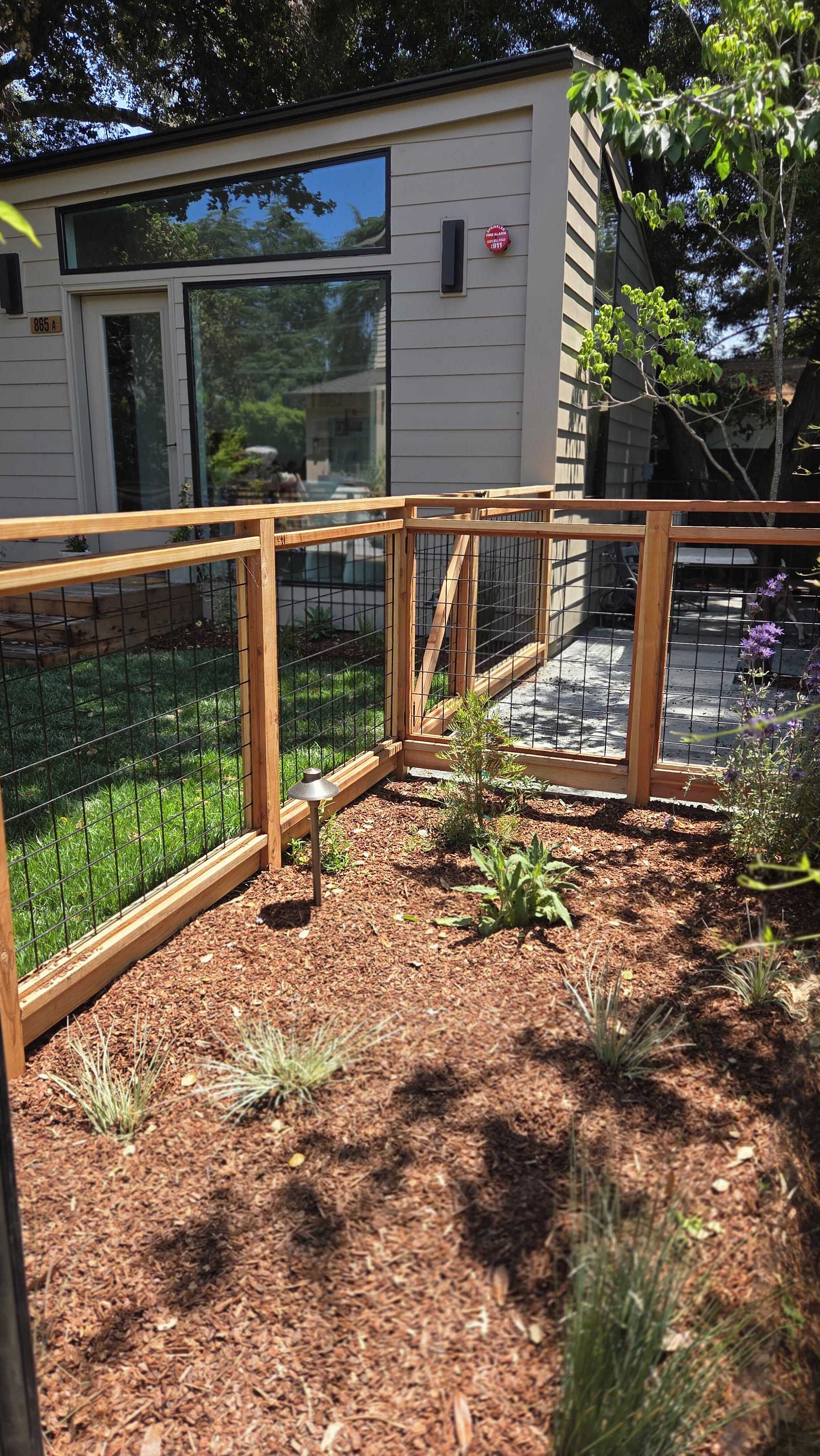 Wood-and-wire garden fence around the lawn and bark planting bed by the detached studio.