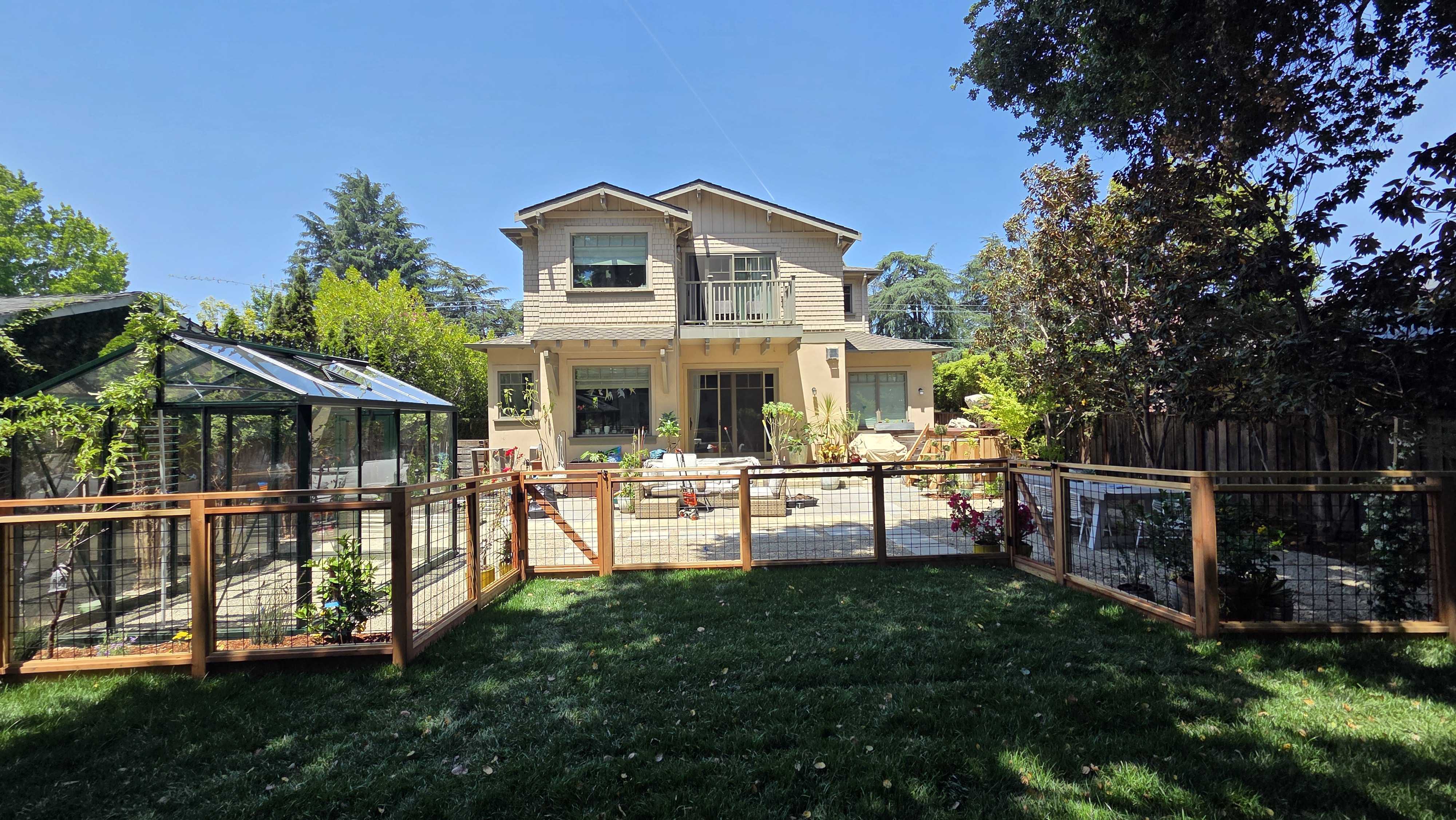 Finished backyard with new lawn, a wood-and-wire garden fence and the glass greenhouse at left.