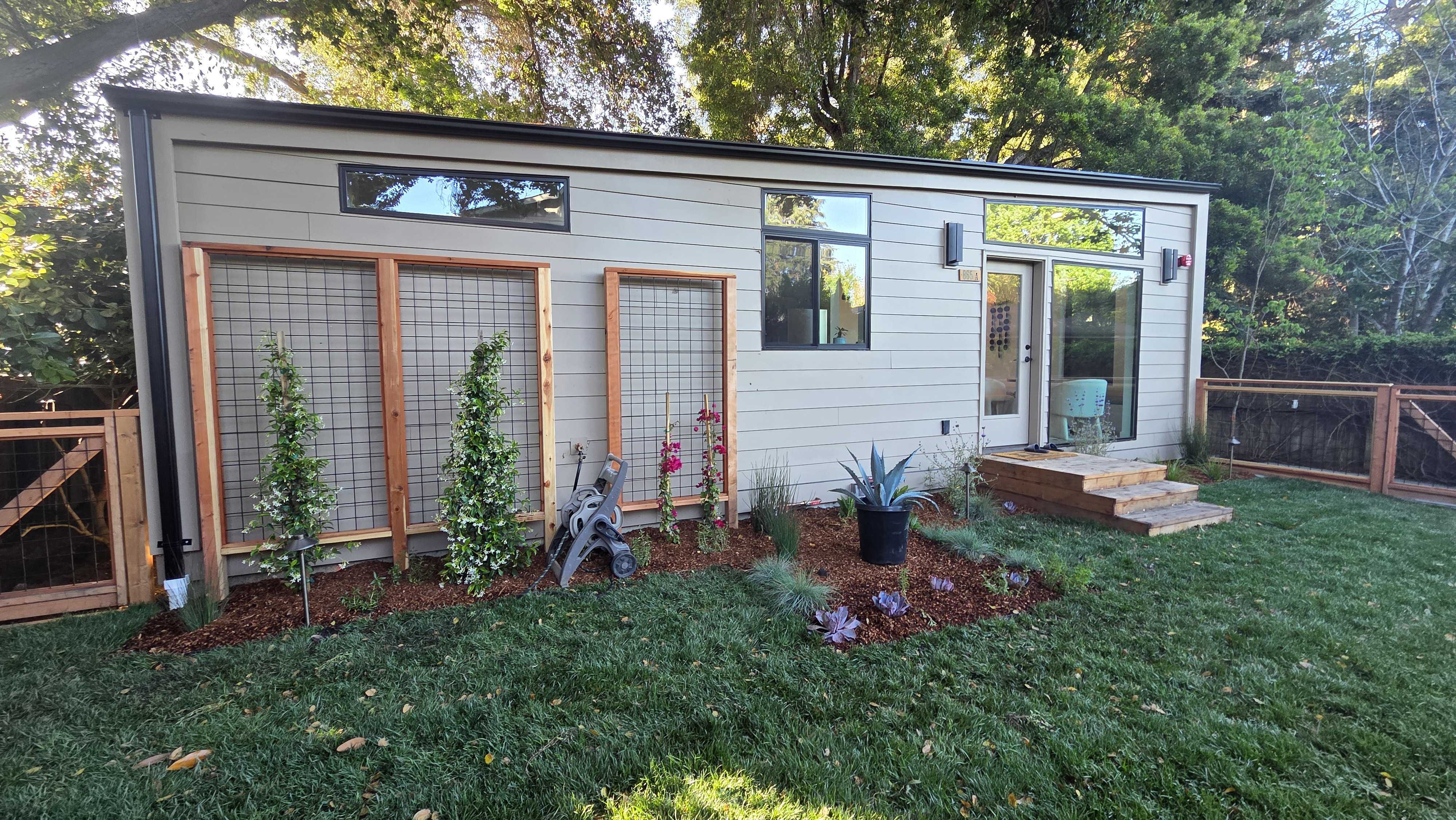 Cedar-framed wire trellises for climbers on the studio wall above a new planting bed and lawn.