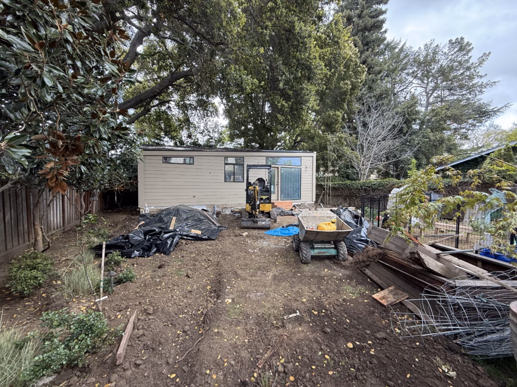 Before — The backyard cleared to bare dirt with an excavator and debris during demolition.