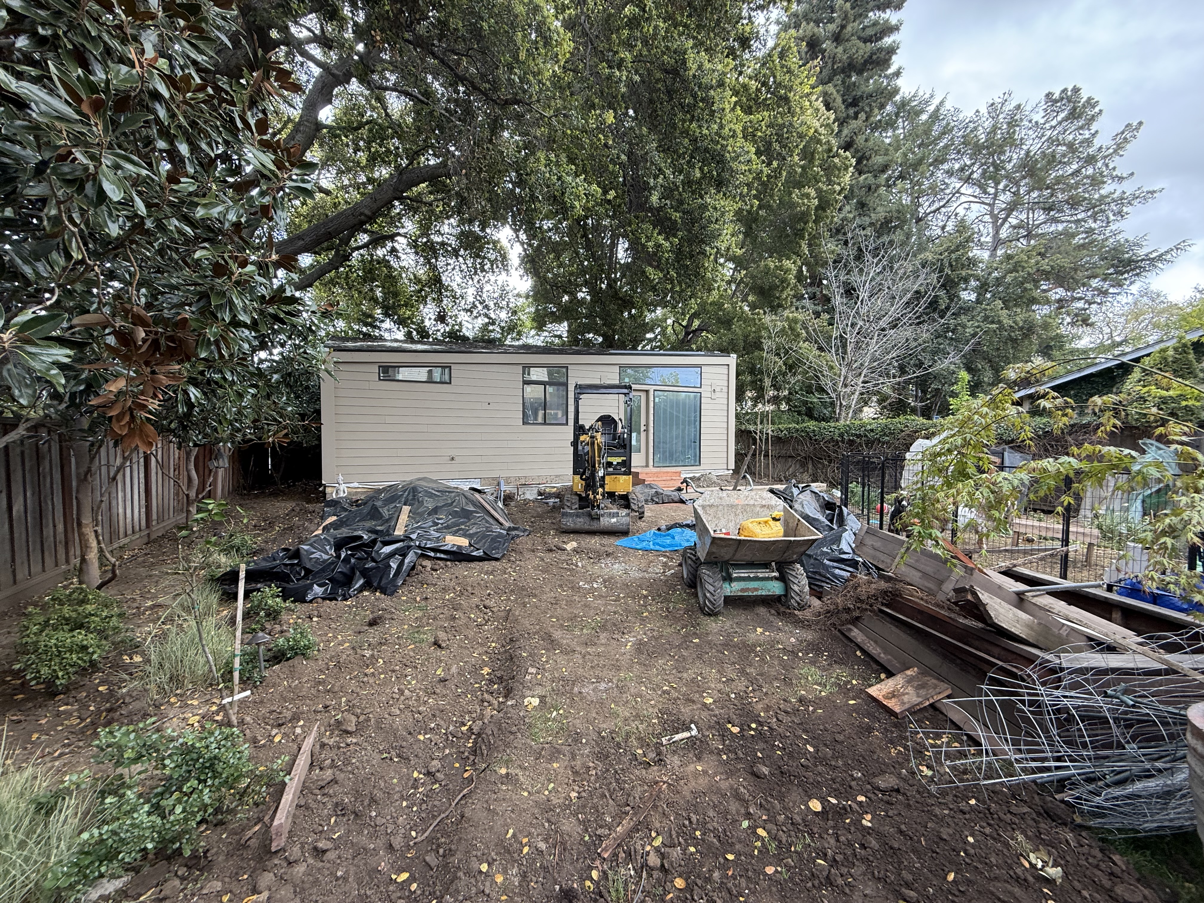 The backyard cleared to bare dirt with an excavator and debris during demolition.