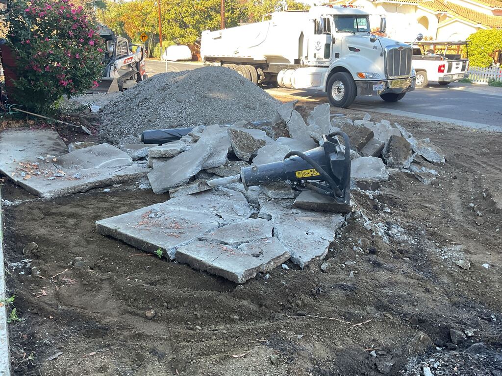Broken concrete slab pieces from a driveway/sidewalk demolition with a handheld demolition hammer lying on top. An...