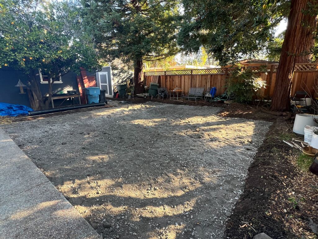Cleared backyard with a compacted granular subbase and graded dirt surface, likely prepared for a future patio or turf...