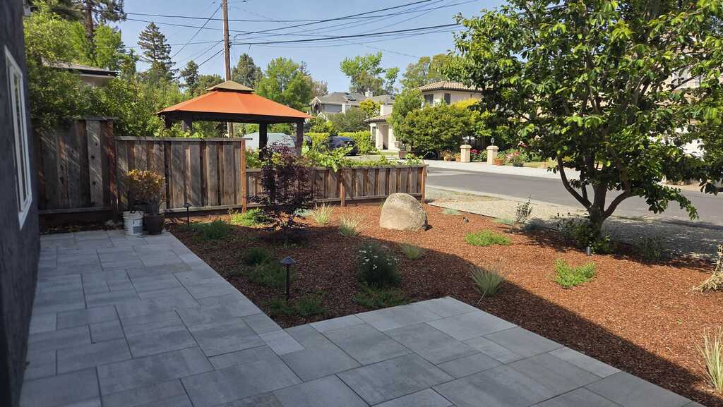 Gray paver patio meeting a bark planting bed with a boulder and new plantings along the wood fence.