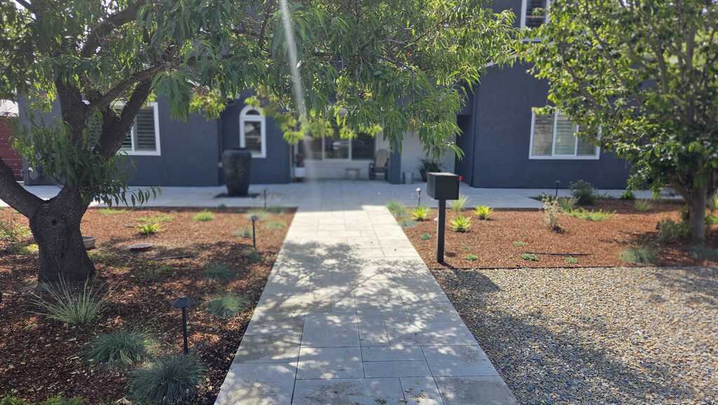 A finished interlocking paver walkway leads to a residential front entry, flanked by mulch beds with recently installed...