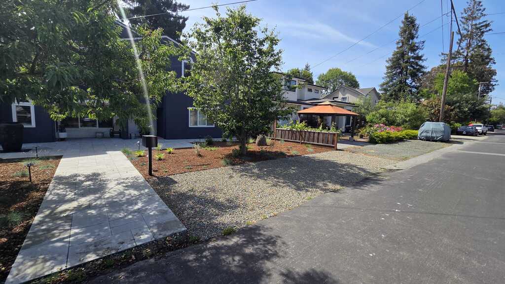 Concrete walkway leads from the sidewalk to the home's entry with adjacent gravel surfacing and mulched planting beds. A...