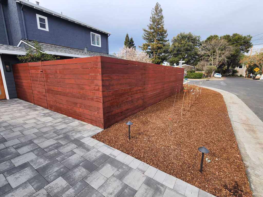 Interlocking gray paver driveway beside a stained horizontal wood fence and a fresh bark planting bed in Palo Alto.