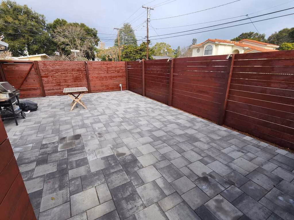 Finished interlocking paver patio in a residential backyard enclosed by a newly stained wooden privacy fence. Pavers are...