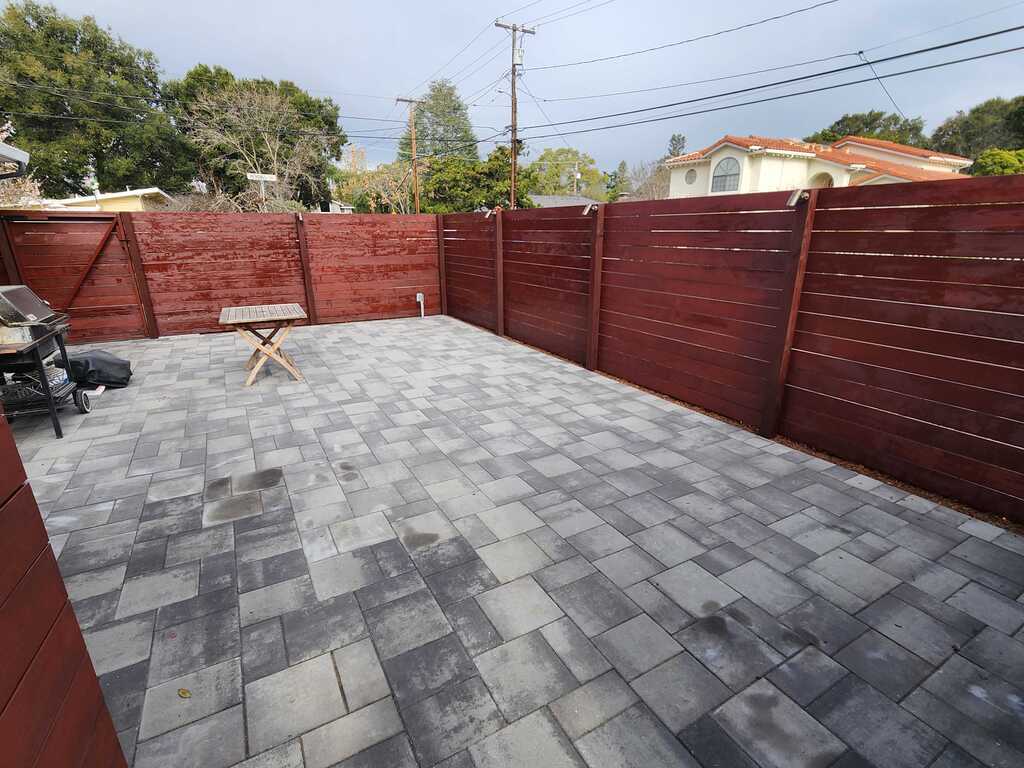 Finished interlocking paver patio in a residential backyard enclosed by a newly stained wooden privacy fence. Pavers are...