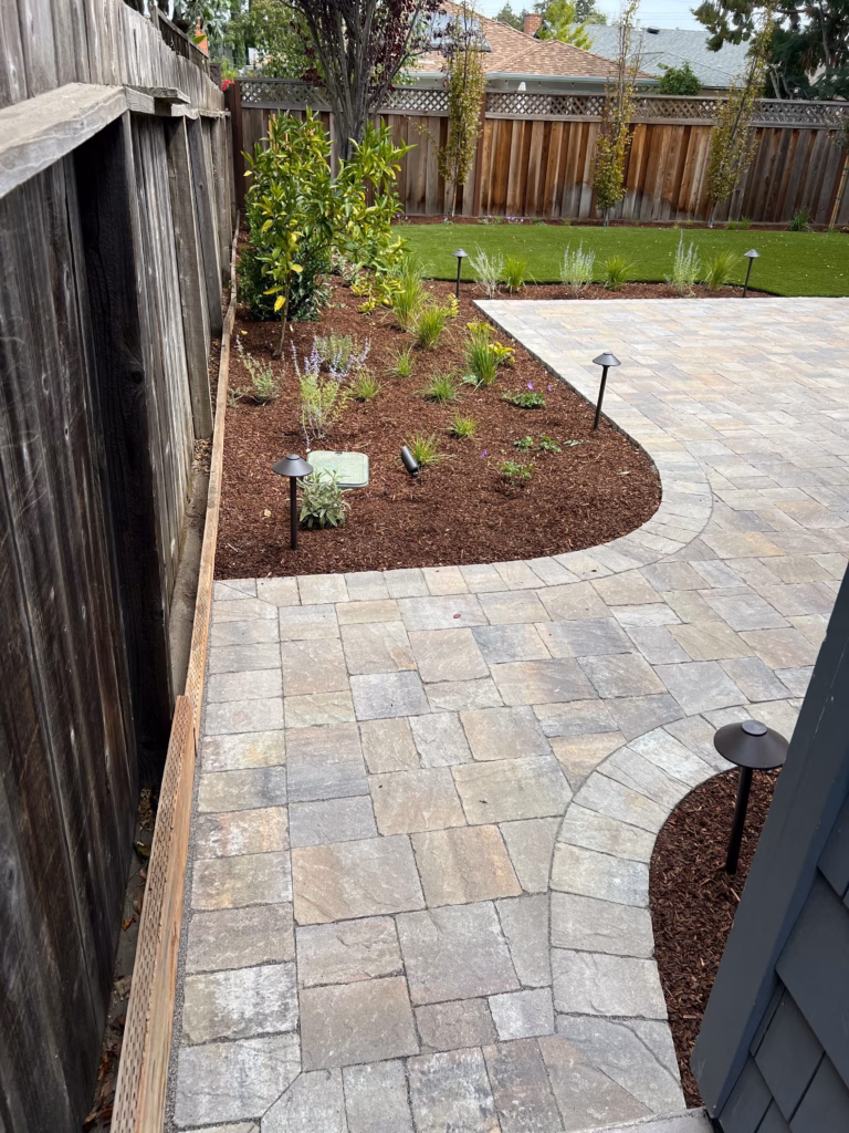 Finished interlocking concrete paver patio and curved walkway laid in a modular ashlar pattern adjacent to newly...