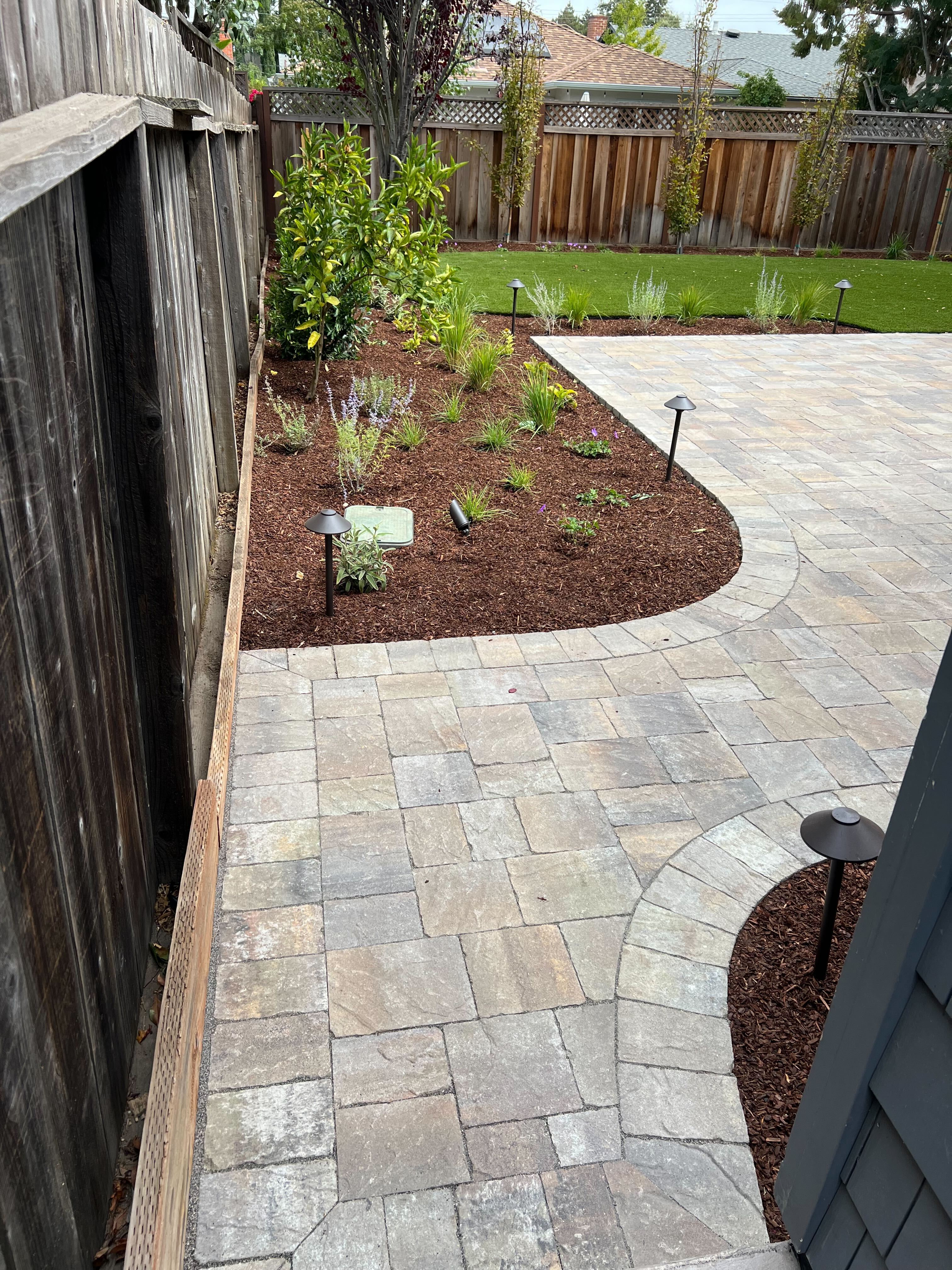 Finished interlocking concrete paver patio and curved walkway laid in a modular ashlar pattern adjacent to newly...