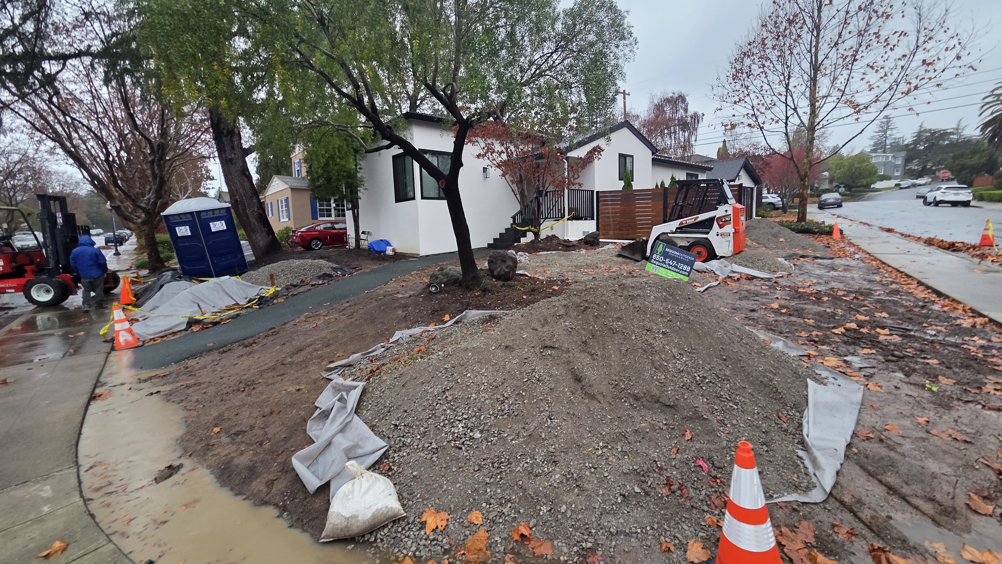 Base-prep stage with stripped front yard, aggregate, equipment, and layout work visible.