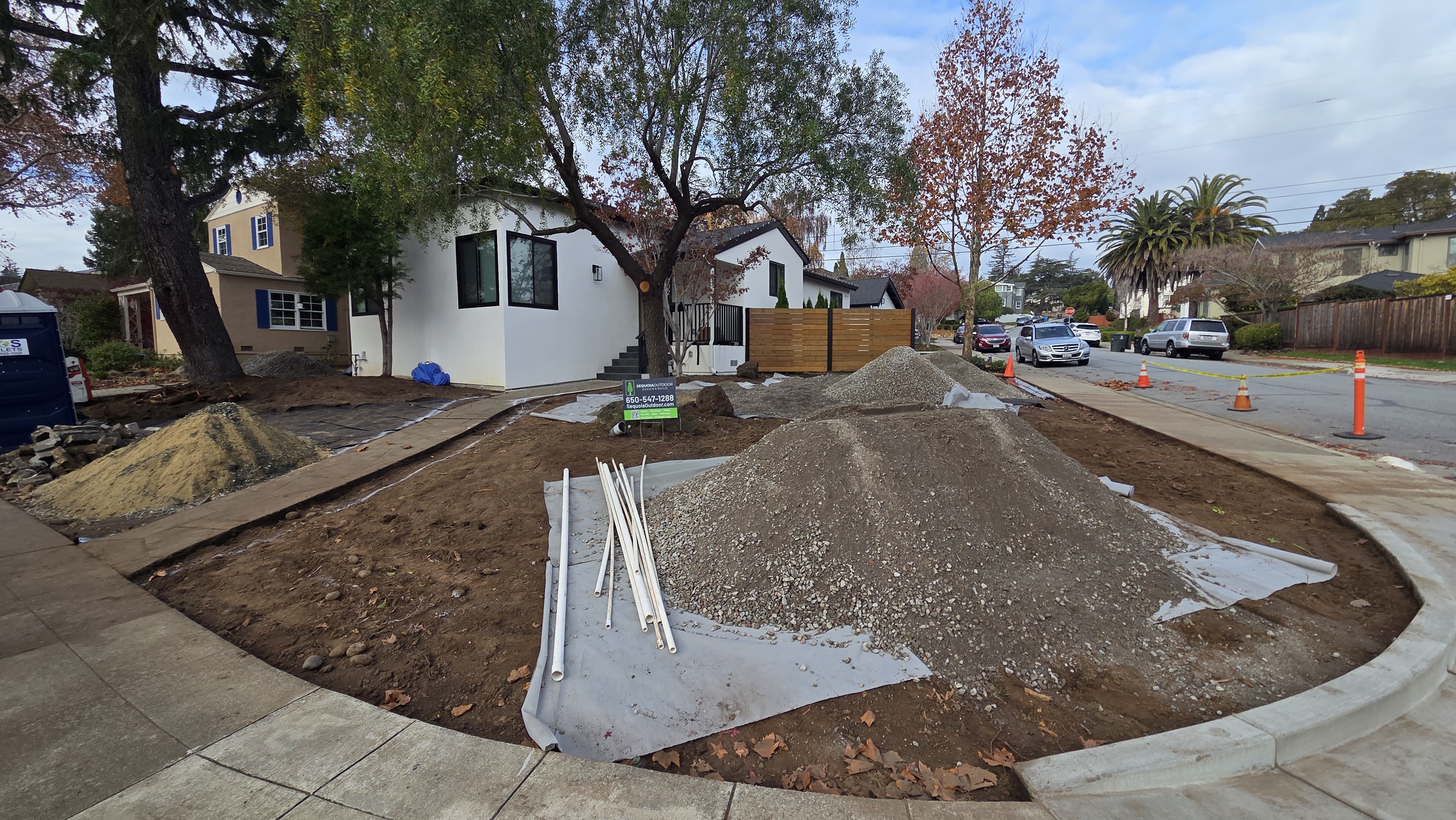 Drainage and base-prep stage showing fabric, aggregate, conduit/drain materials, and grading work.