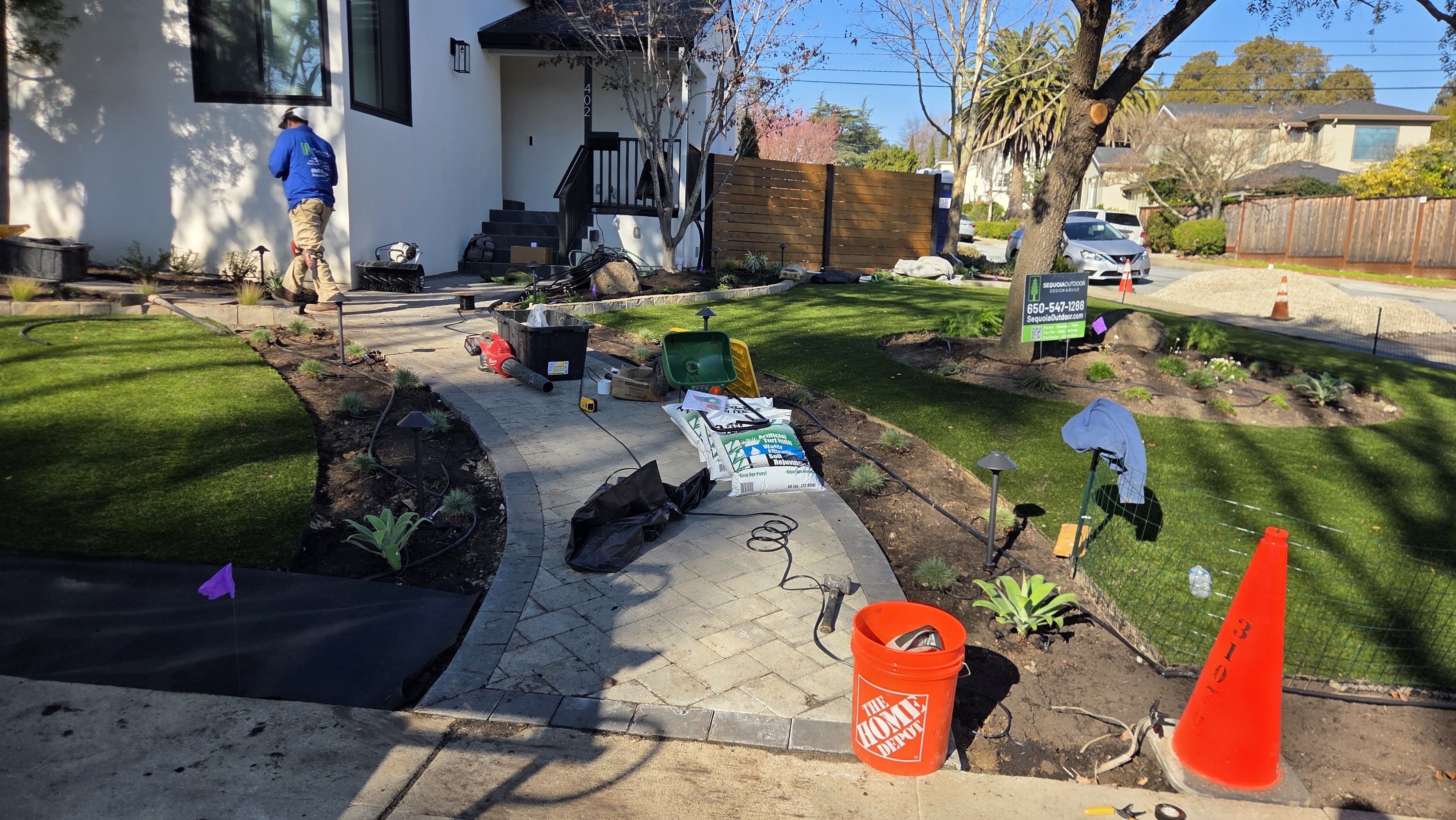 Active install stage showing paver walkway, turf, planting layout, tools, and crew activity.