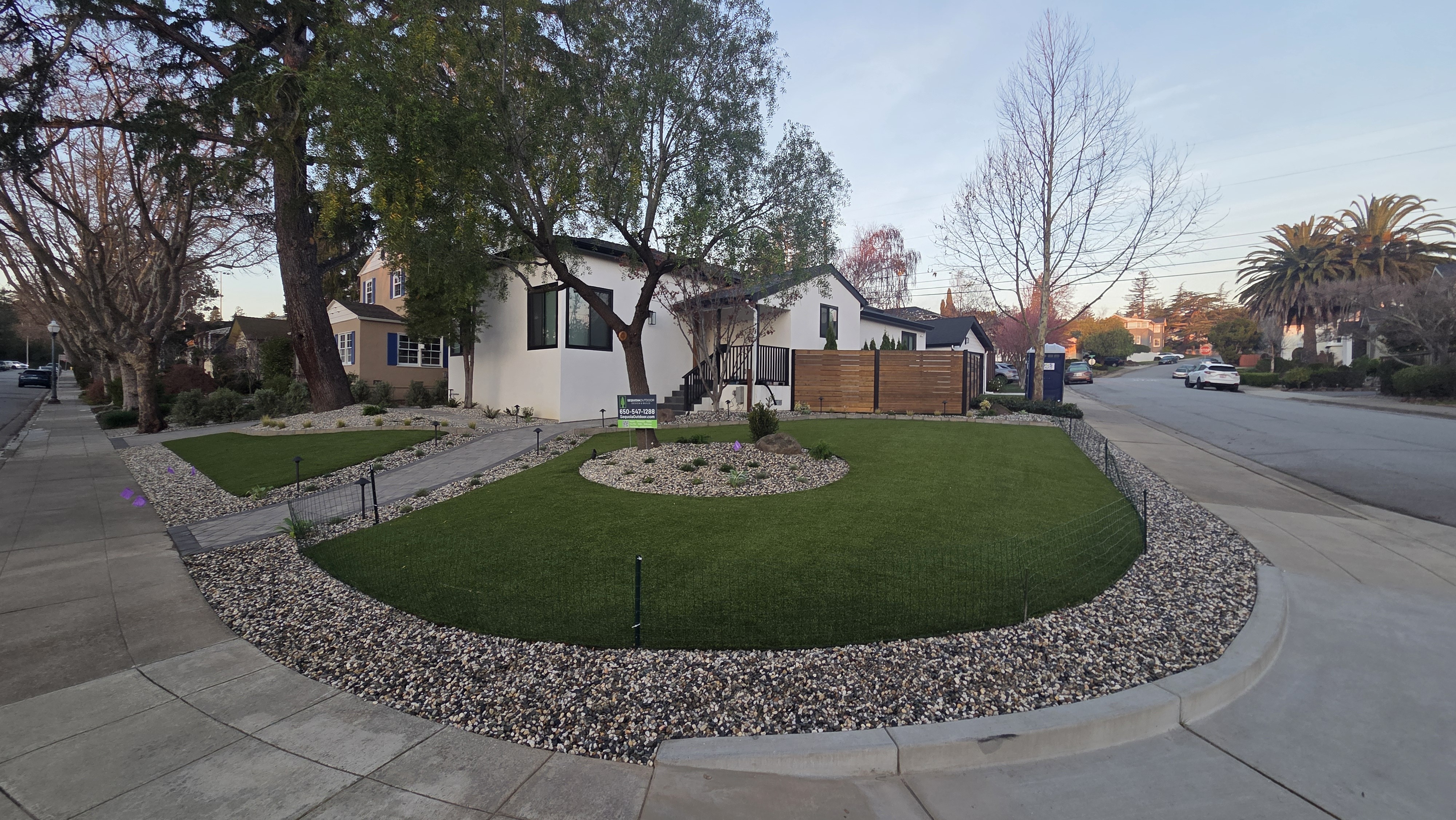 Wide finished front-yard view showing the strongest complete paver, turf, rock, planting, lighting, and curb-appeal...