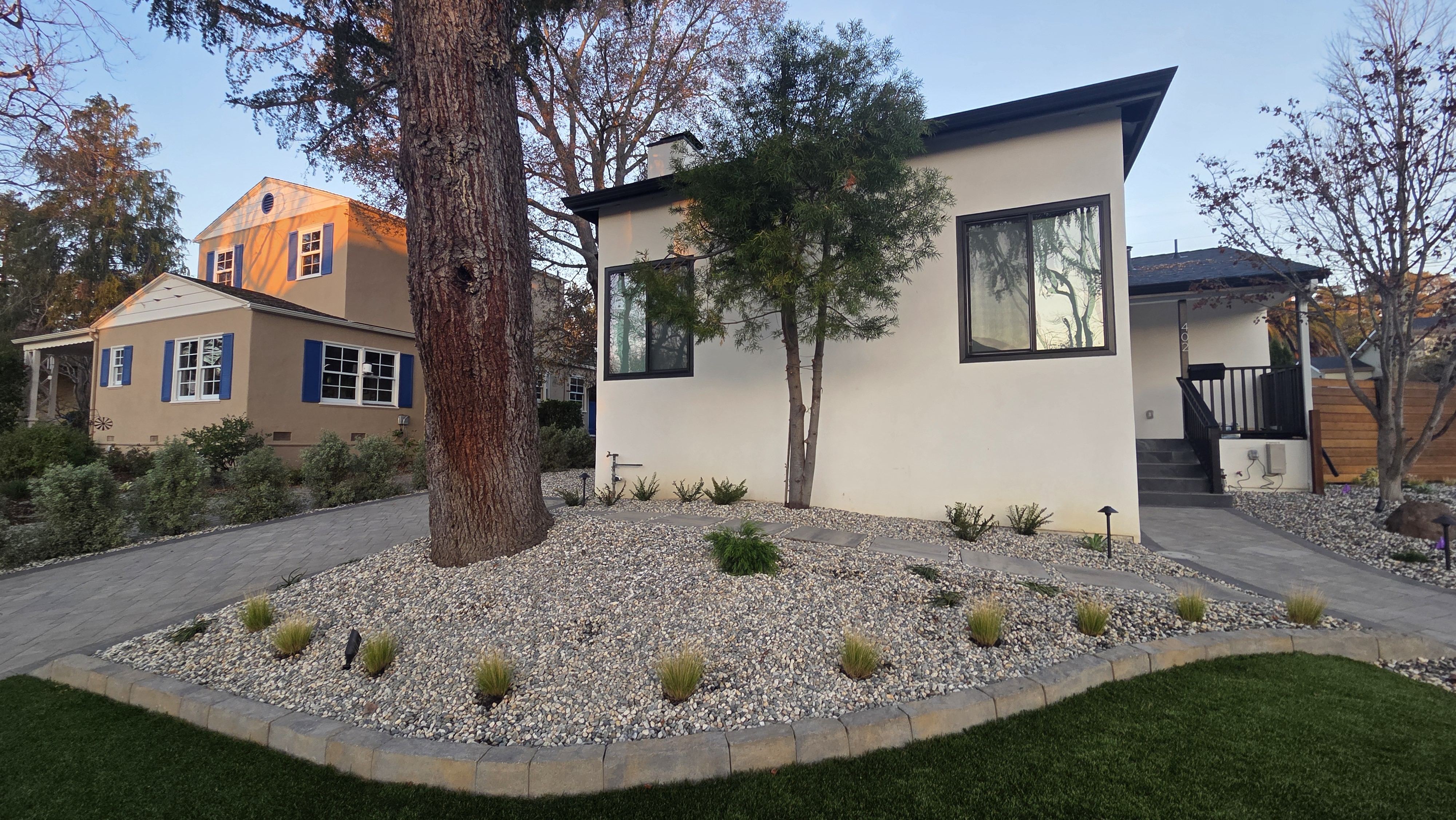 Finished front/driveway angle showing paver walkway, driveway transition, decorative rock, turf, and planting. No active...