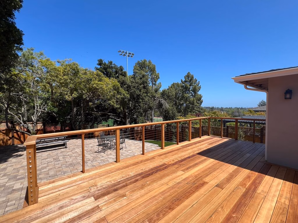 New redwood deck with horizontal cable railing overlooking the paver patio and mature tree line.