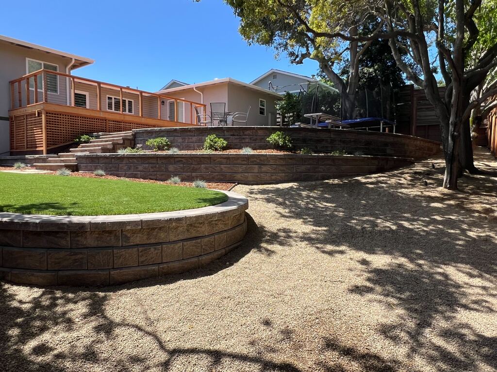 Two tiers of curved segmental retaining wall lift the turf lawn and planting beds above a decomposed-granite area.