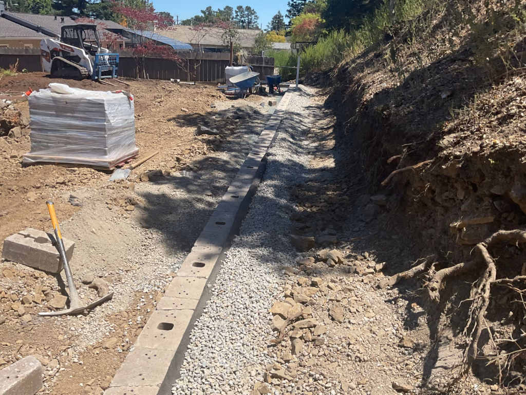 Segmental retaining wall under construction along the hillside slope, partway up to finish height