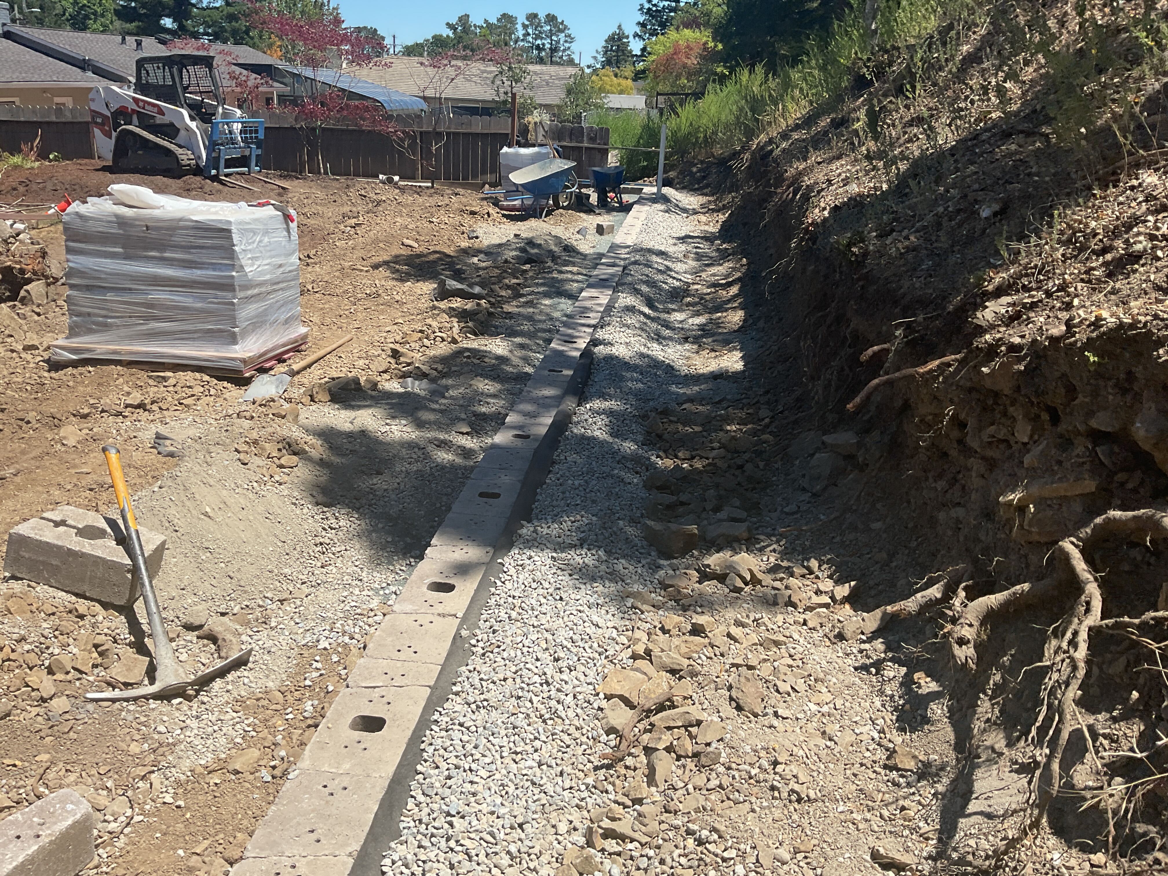Segmental retaining wall under construction along the hillside slope, partway up to finish height
