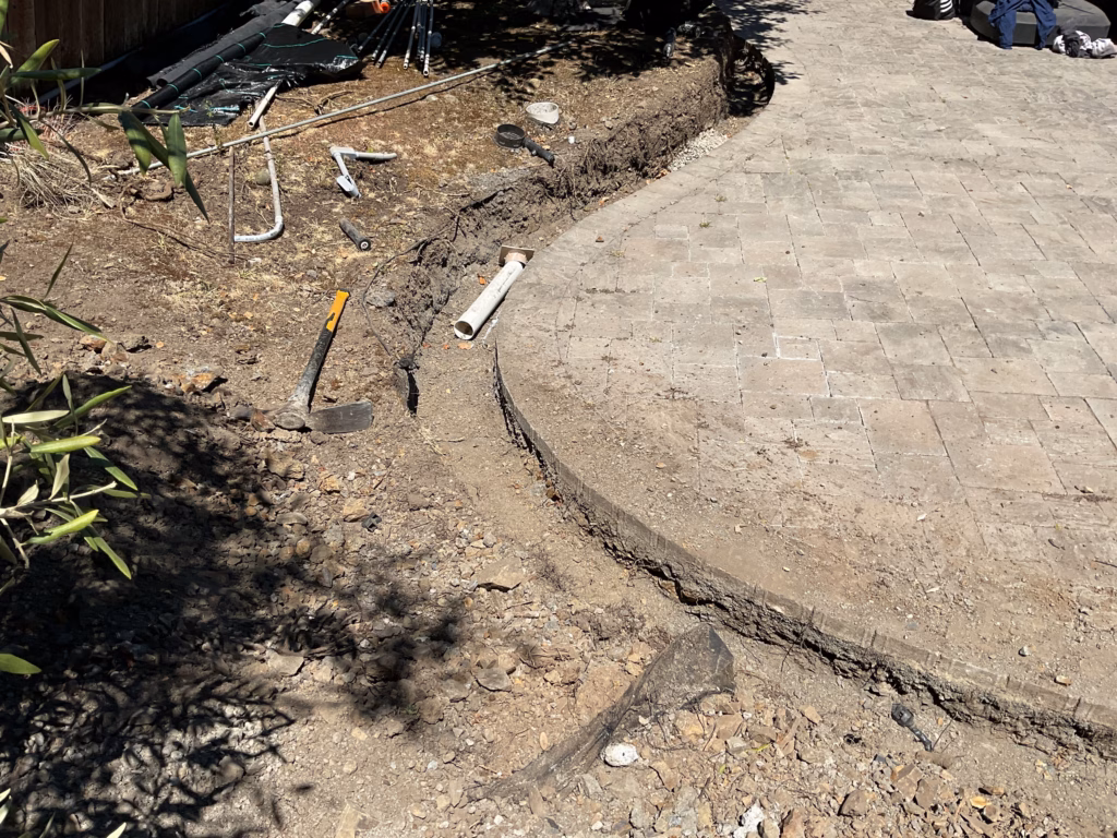 Curved interlocking paver patio partially installed with exposed perimeter trench at the edge