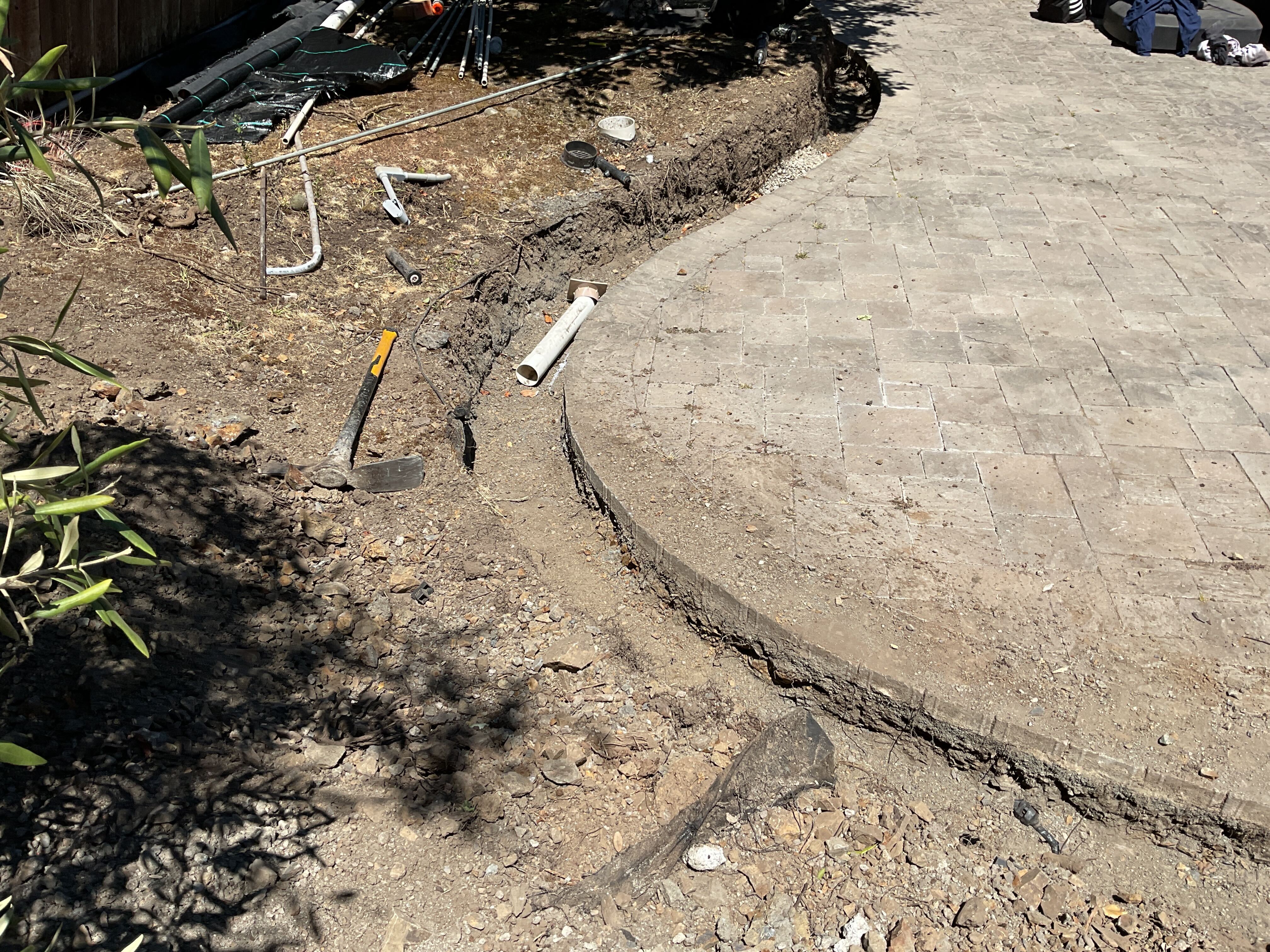 Curved interlocking paver patio partially installed with exposed perimeter trench at the edge