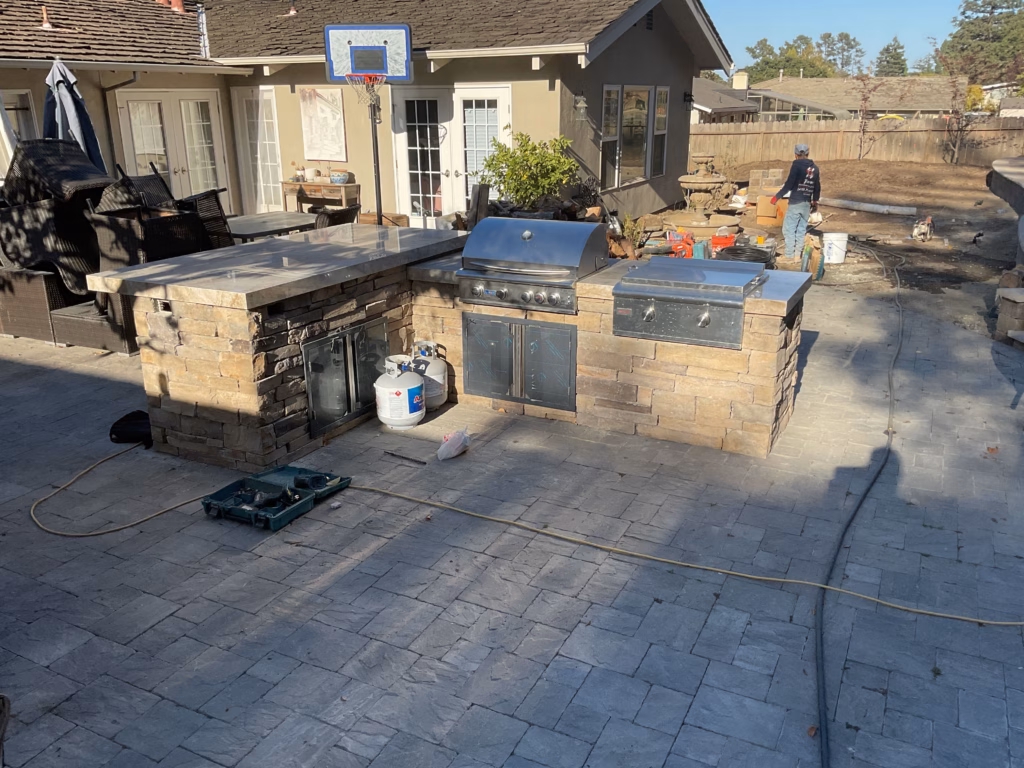 Outdoor kitchen island with built-in grill being assembled on the new paver patio