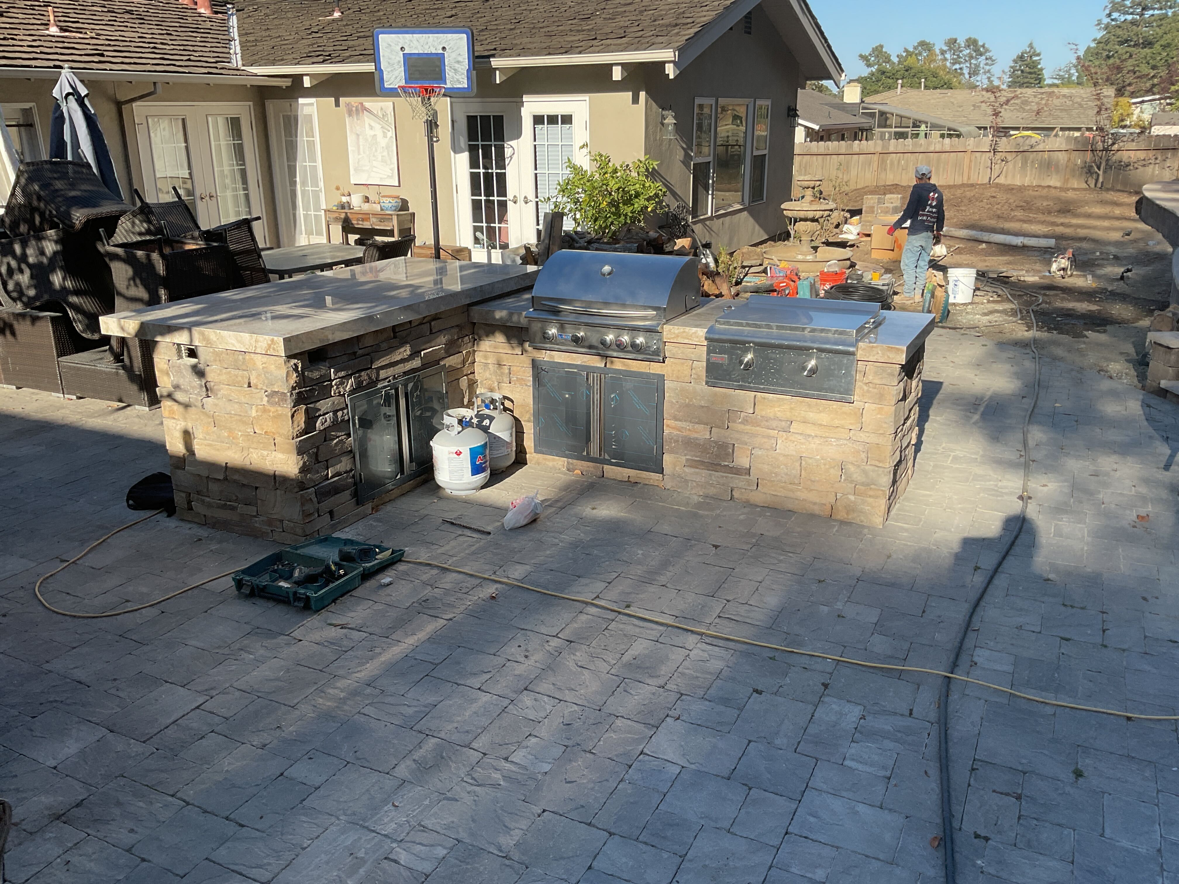 Outdoor kitchen island with built-in grill being assembled on the new paver patio