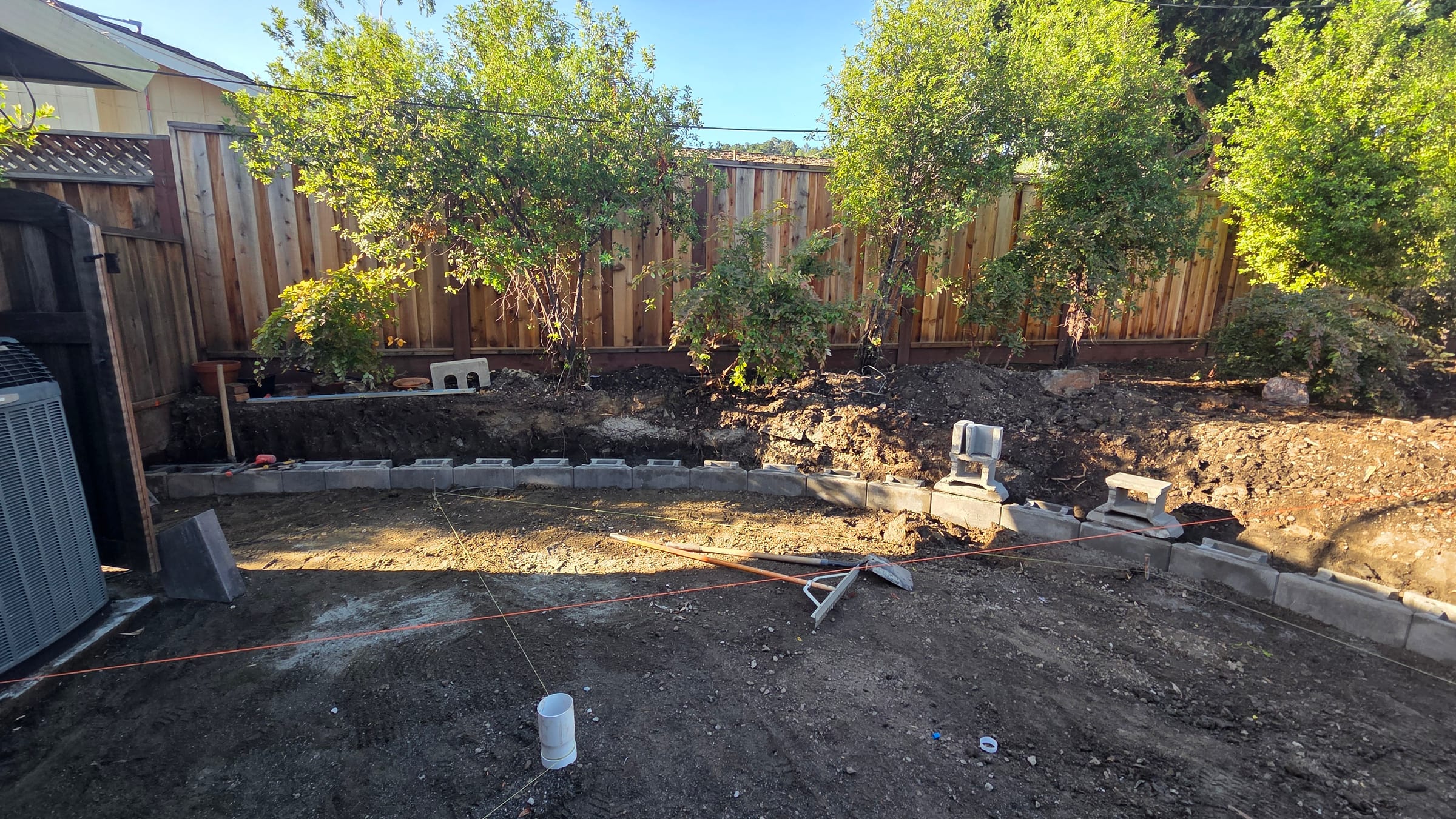 Compacted aggregate base with starter retaining-wall blocks along the rear fence during patio layout.