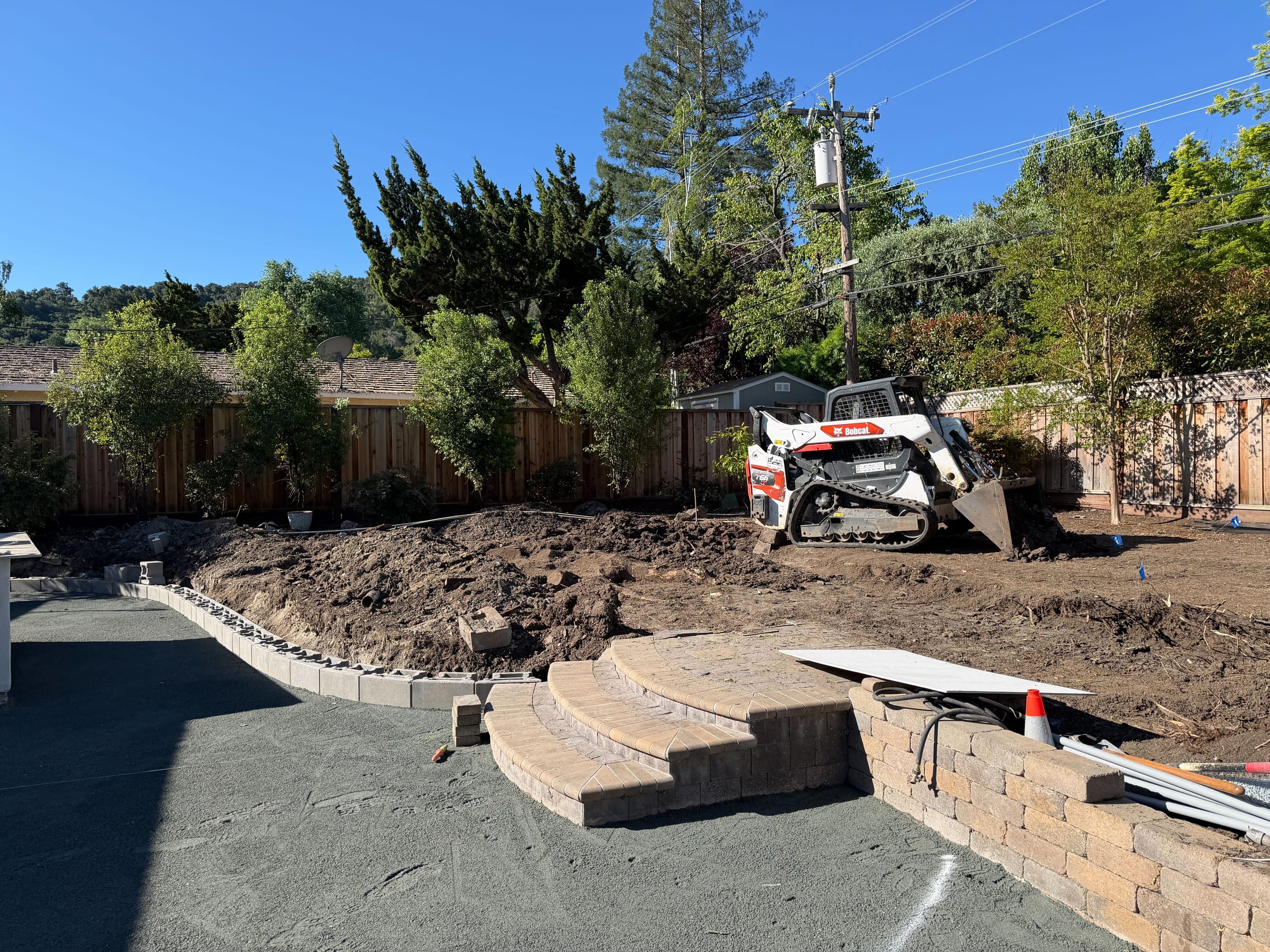 Curved paver steps and block retaining wall taking shape during active hardscape installation.