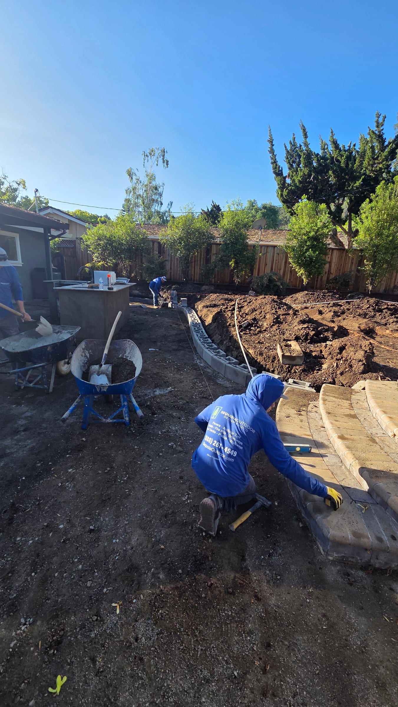 Crew setting block on the curved retaining wall beside the outdoor kitchen island.
