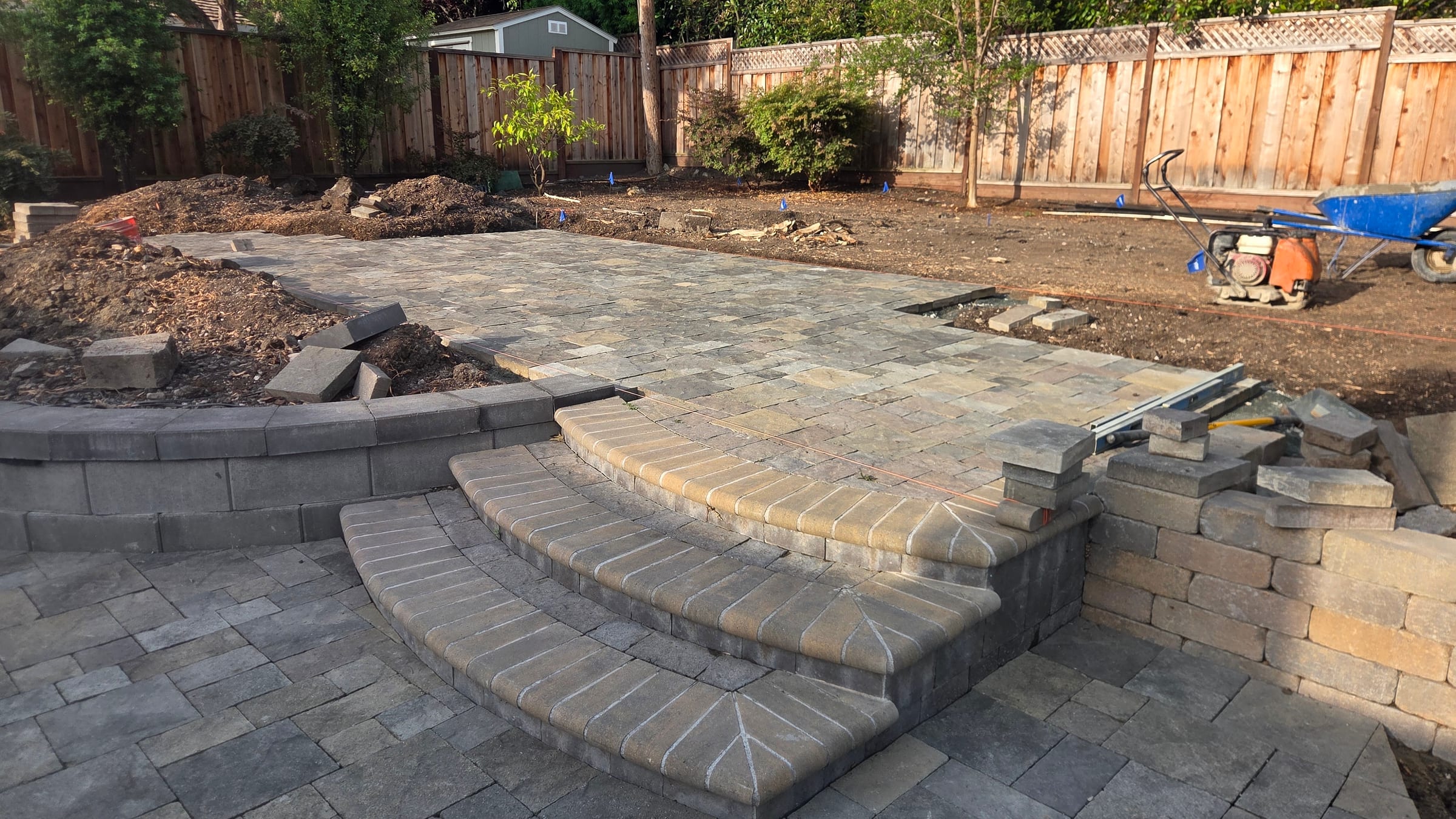 Curved paver steps, raised paver landing, and block planter walls near final hardscape completion.