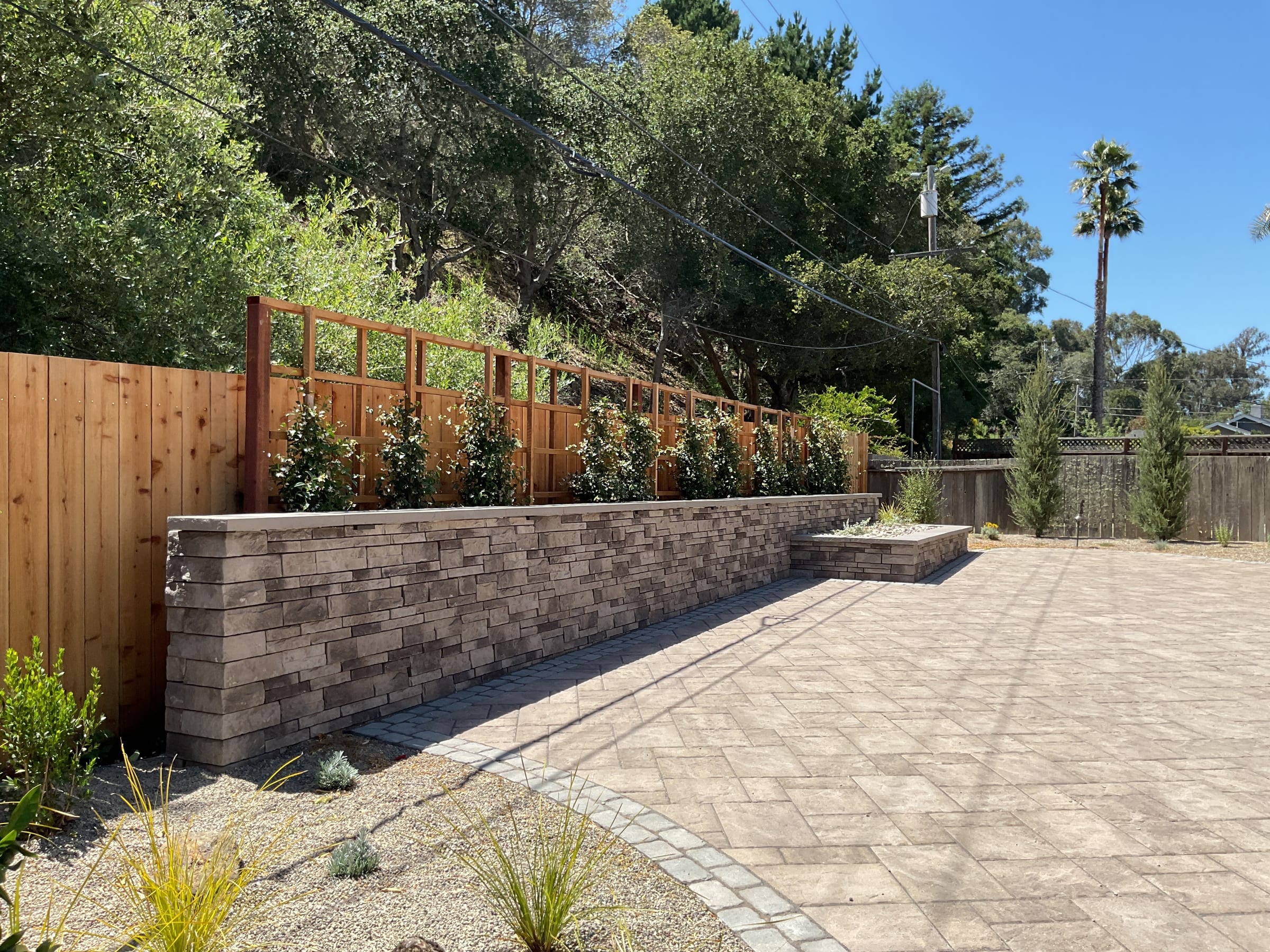 Wide paver patio and capped stone retaining wall with a wood fence trellis and new planting bed.