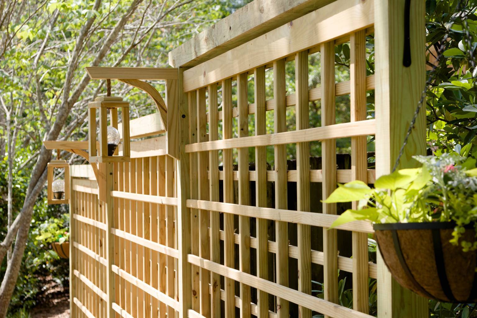 Two lantern-style path lights hang from a cedar trellis panel beside a hanging basket planter.
