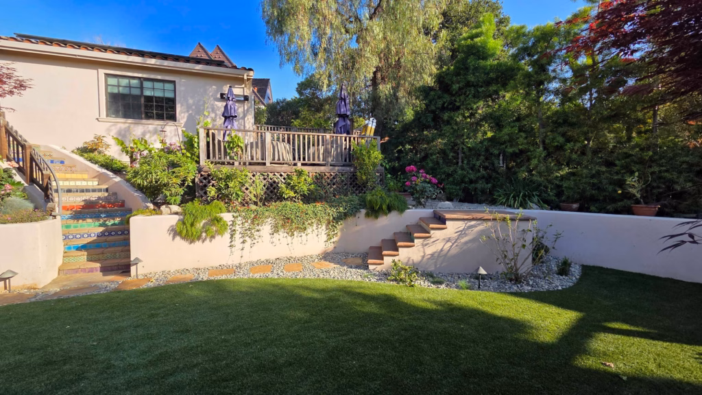 Turf lawn leading to mosaic steps, river-rock borders, and stucco retaining walls.