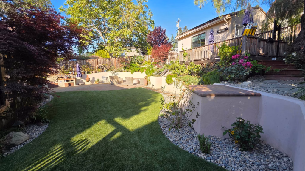 Artificial turf lawn, paver patio, and capped stucco retaining wall in the finished backyard.