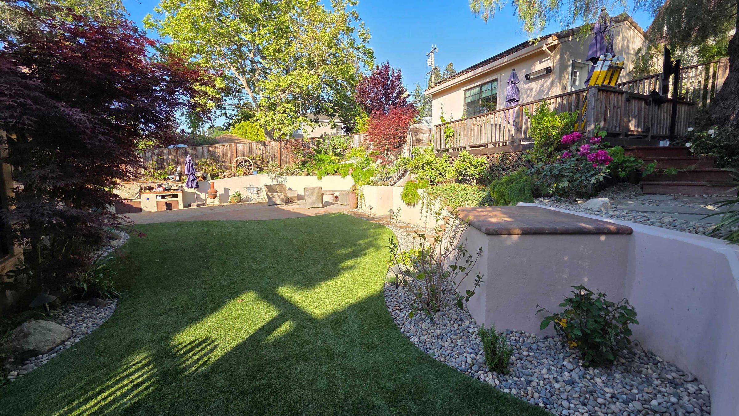 Artificial turf lawn, paver patio, and capped stucco retaining wall in the finished backyard.
