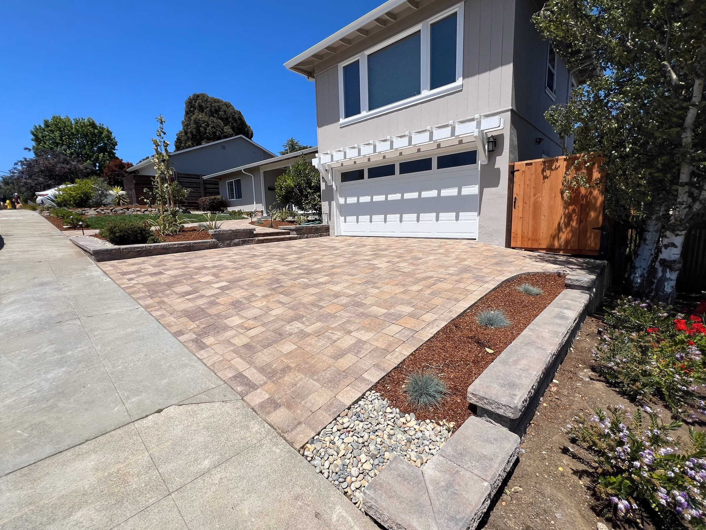 New paver driveway leading to the garage, edged by a capped segmental wall, river rock and fresh front-yard planting in San Mateo.