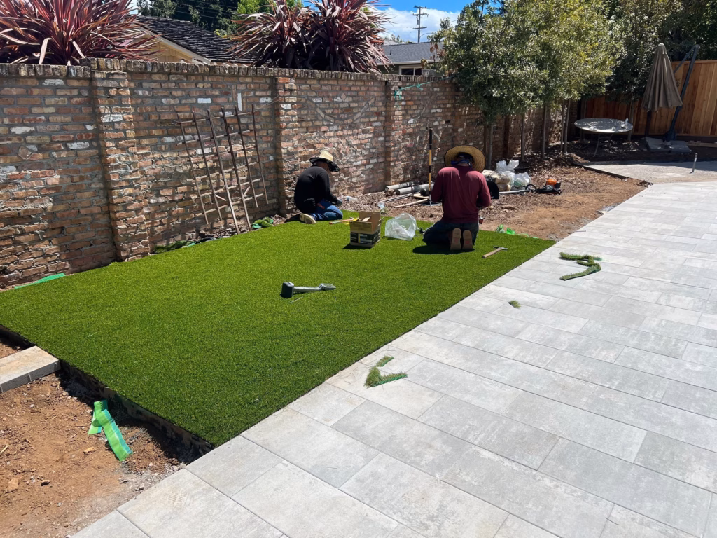 Synthetic turf lawn being fitted between paver deck and planting beds in Los Altos, CA