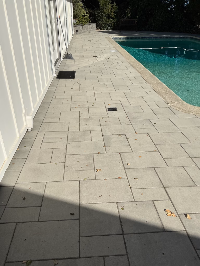 After — light gray paver walk between the same building and the pool, with drain grates set in the paving