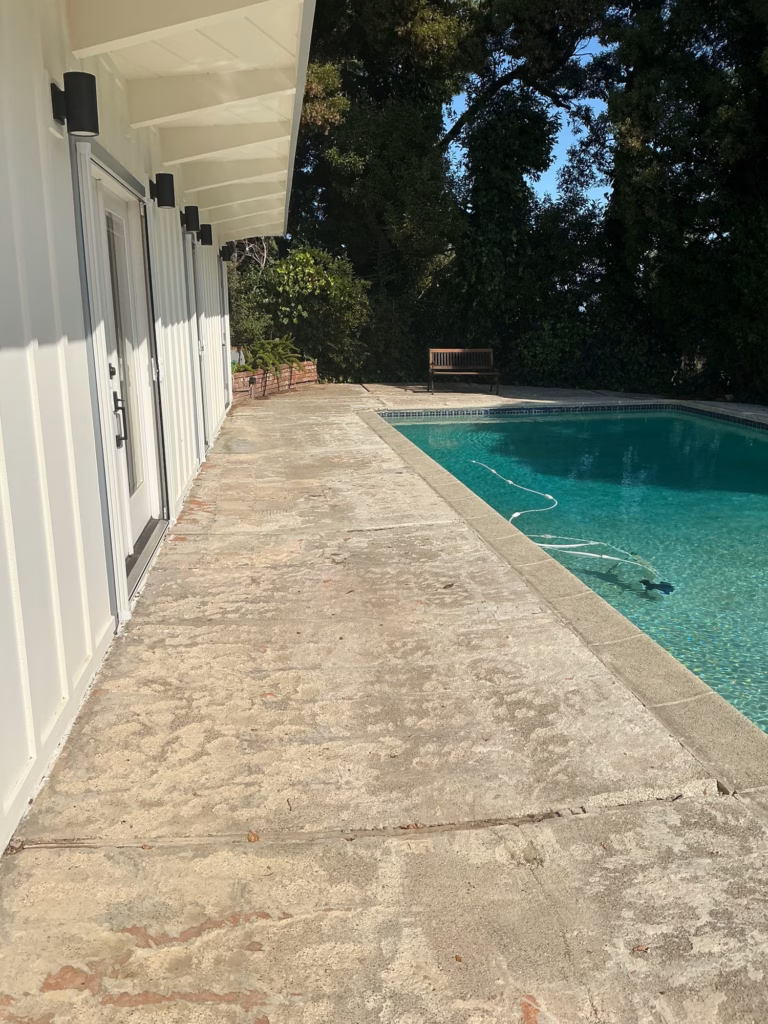 Before — cracked, stained concrete walk between a white board-and-batten building and a pool in Hillsborough