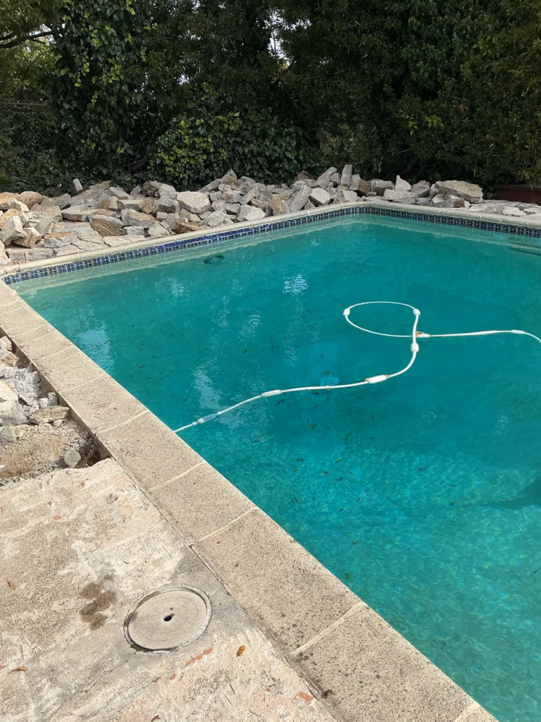 Broken-out concrete piled at the far end of a pool in Hillsborough, with the coping still in place