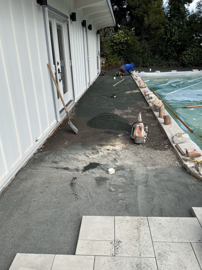 First light gray pavers set at the end of a prepared walk along a board-and-batten building, pool under cover at right
