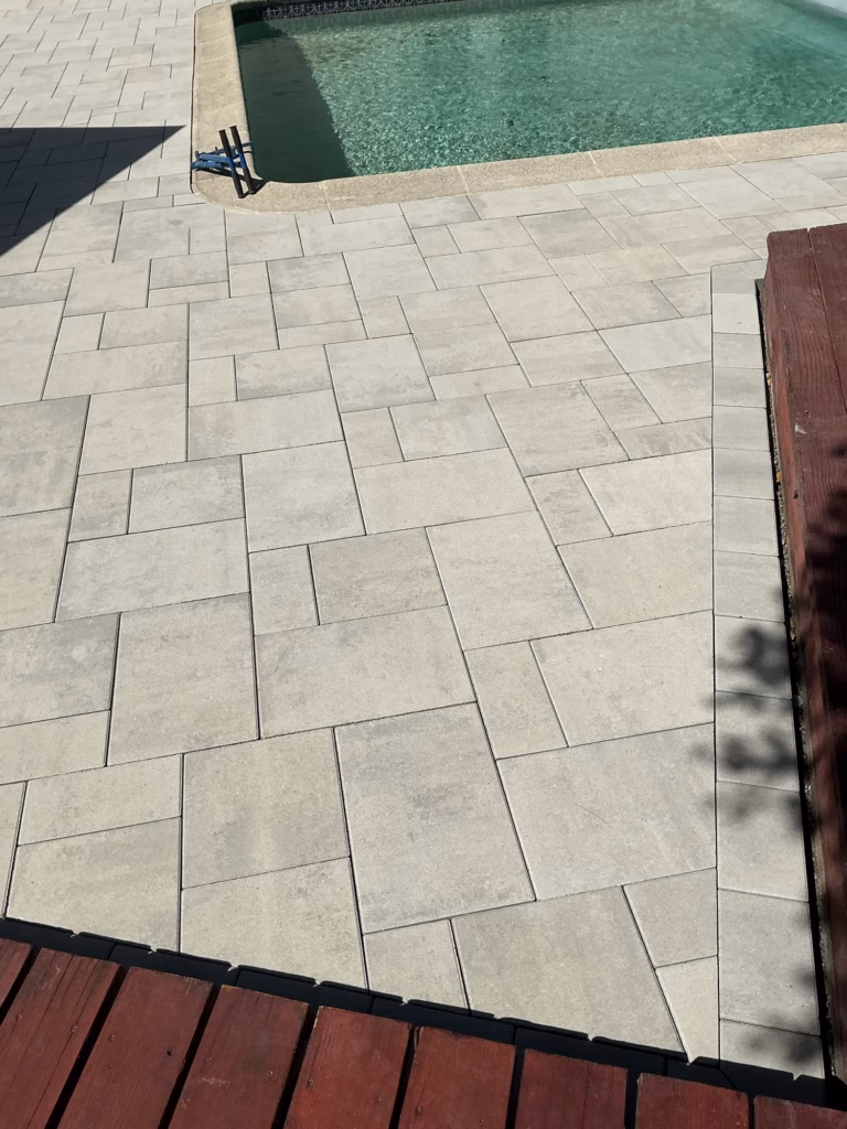 Light gray pavers fitted between a pool corner and the edges of a red-stained wood deck