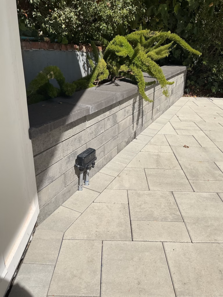 New gray Belgard Melville wall with a dark cap holding a raised planter of ferns, new pavers along its base
