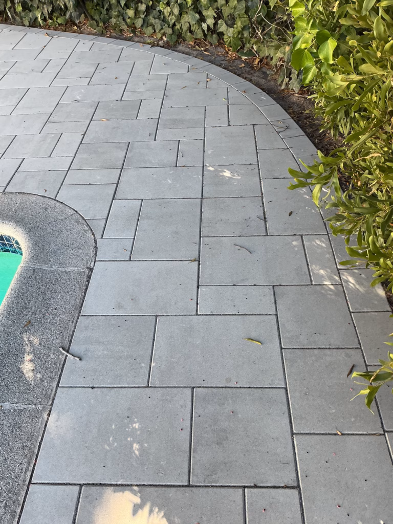 Light gray pavers curving with the rounded corner of a pool beside a hedge
